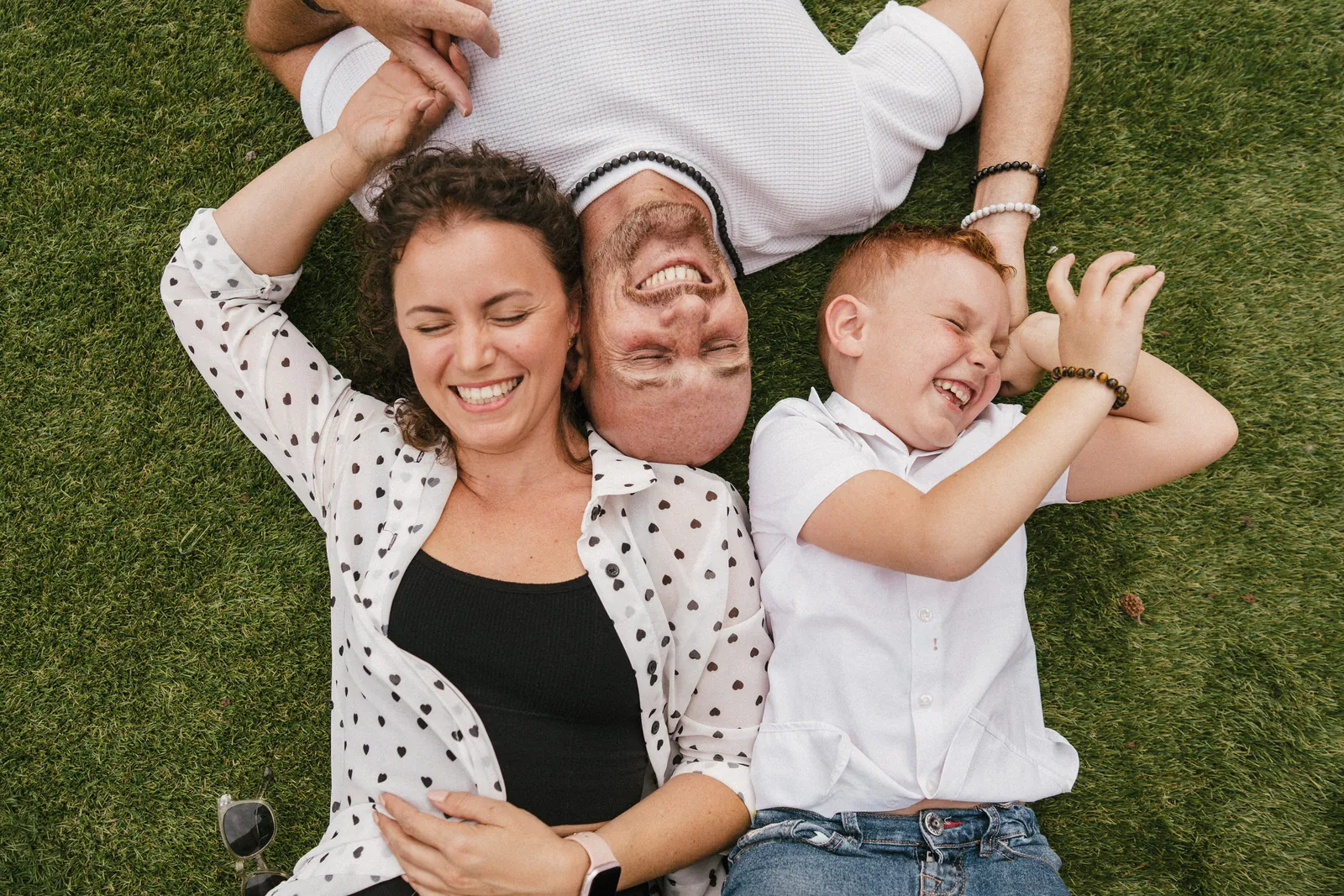 Allongés tête-bêche dans l'herbe, maman, papa et leur fils rient aux éclats