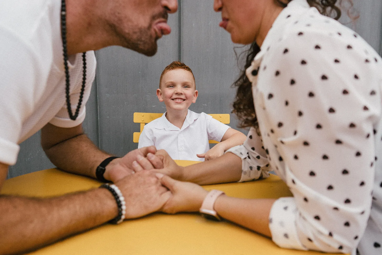 Les parents tirent la langue au-dessus d'une table jaune, leur fils éclate de rire entre eux
