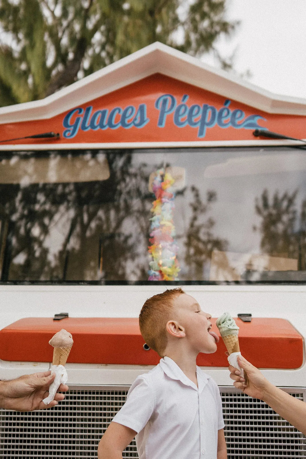 Devant un camion de glaces orange, un garçon lèche un cornet tendu par ses parents