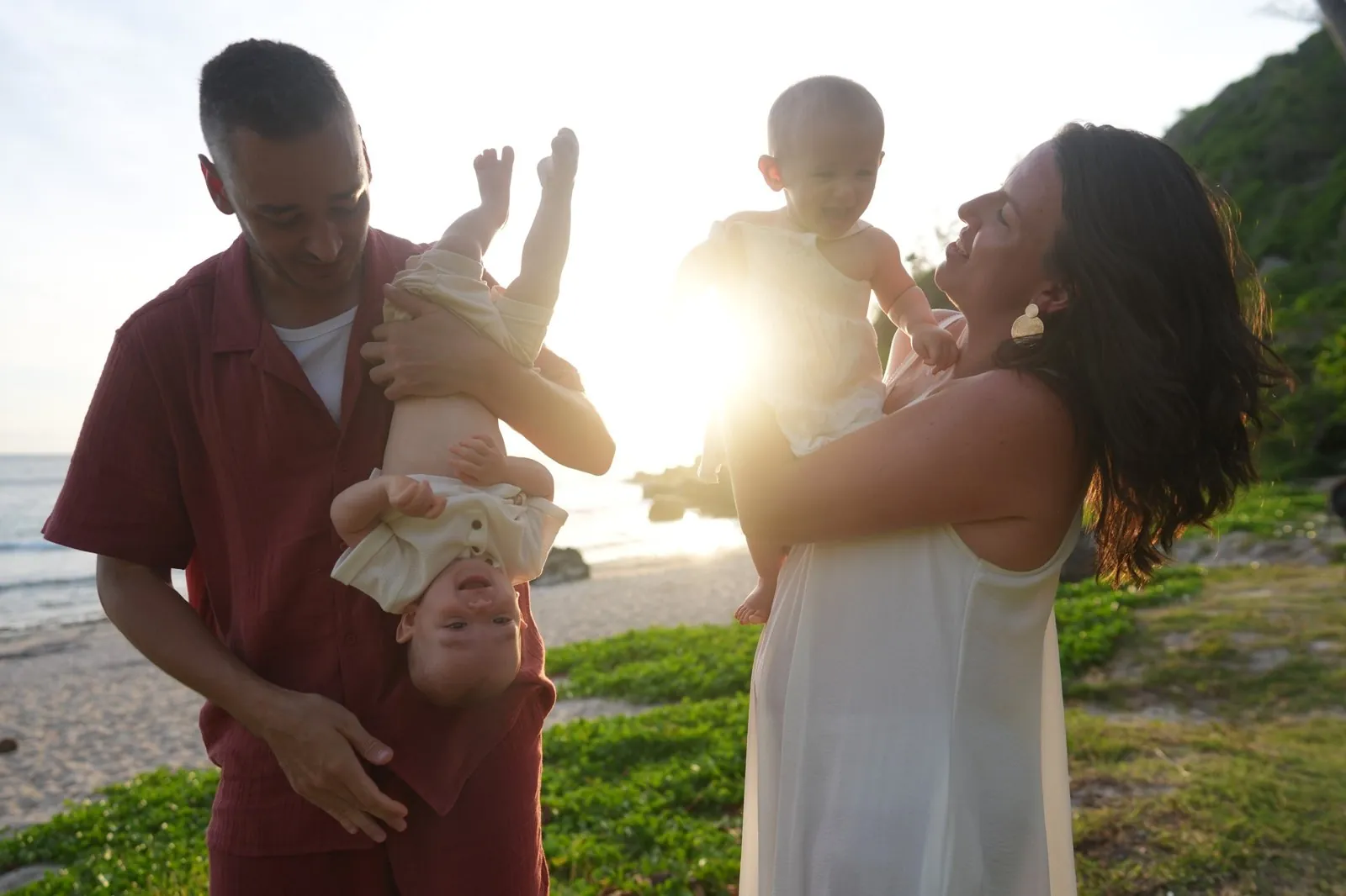 Sur la plage au coucher du soleil, un papa tient son bébé la tête en bas
